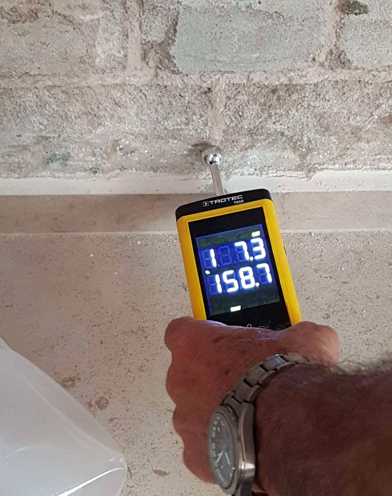 A pin moisture meter held against a masonry wall. Shown on the homepage for Rochester, NY.